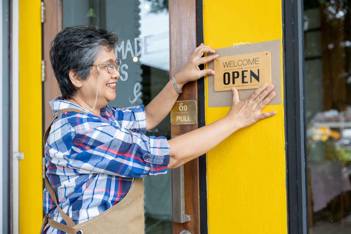 Senior woman putting sigh Open on a wall of her cafe