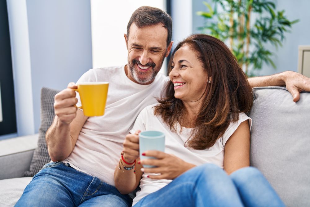 Middle age man and woman couple drinking coffee sitting on sofa at home